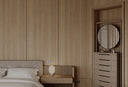 Schlafzimmer mit Wandpaneelen in Holzoptik, Bett, Kommode und kleiner Schrank mit Spiegel