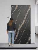 Eine junge Frau steht vor einem Wandpaneel in Marmoroptik Black Marquina.