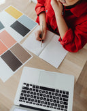 Frau arbeitet am Schreibtisch, notiert auf Block, Laptop und Farbmuster liegen bereit